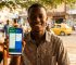 Jeune entrepreneur ivoirien à Abidjan utilisant ChatGPT sur son smartphone pour rédiger un post Facebook