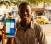 Jeune entrepreneur ivoirien à Abidjan utilisant ChatGPT sur son smartphone pour rédiger un post Facebook