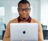 Jeune entrepreneur africain à lunettes tenant un MacBook dans un bureau moderne lumineux