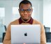 Jeune entrepreneur africain à lunettes tenant un MacBook dans un bureau moderne lumineux