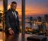 Un entrepreneur pose son téléphone face contre son bureau, devant la baie vitrée d'une tour d'Abidjan au crépuscule